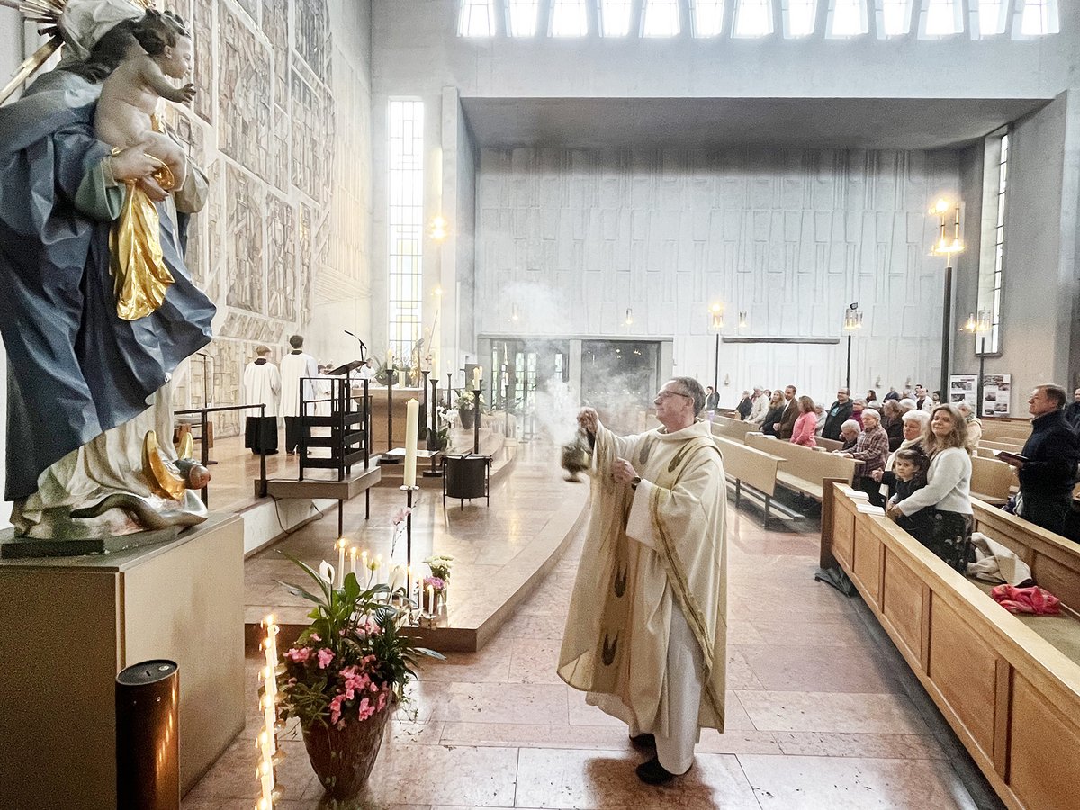 Priester schwenkt Weihrauchfass bei Gottesdienst, im Vordergrund Marienstatue, im Hintergrund Gemeinde in moderner Kirche.