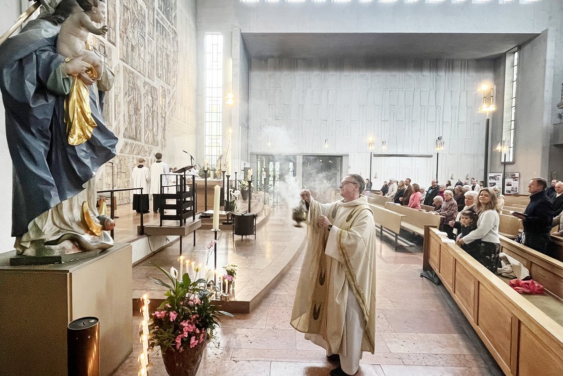 Priester schwenkt Weihrauchfass bei Gottesdienst, im Vordergrund Marienstatue, im Hintergrund Gemeinde in moderner Kirche.