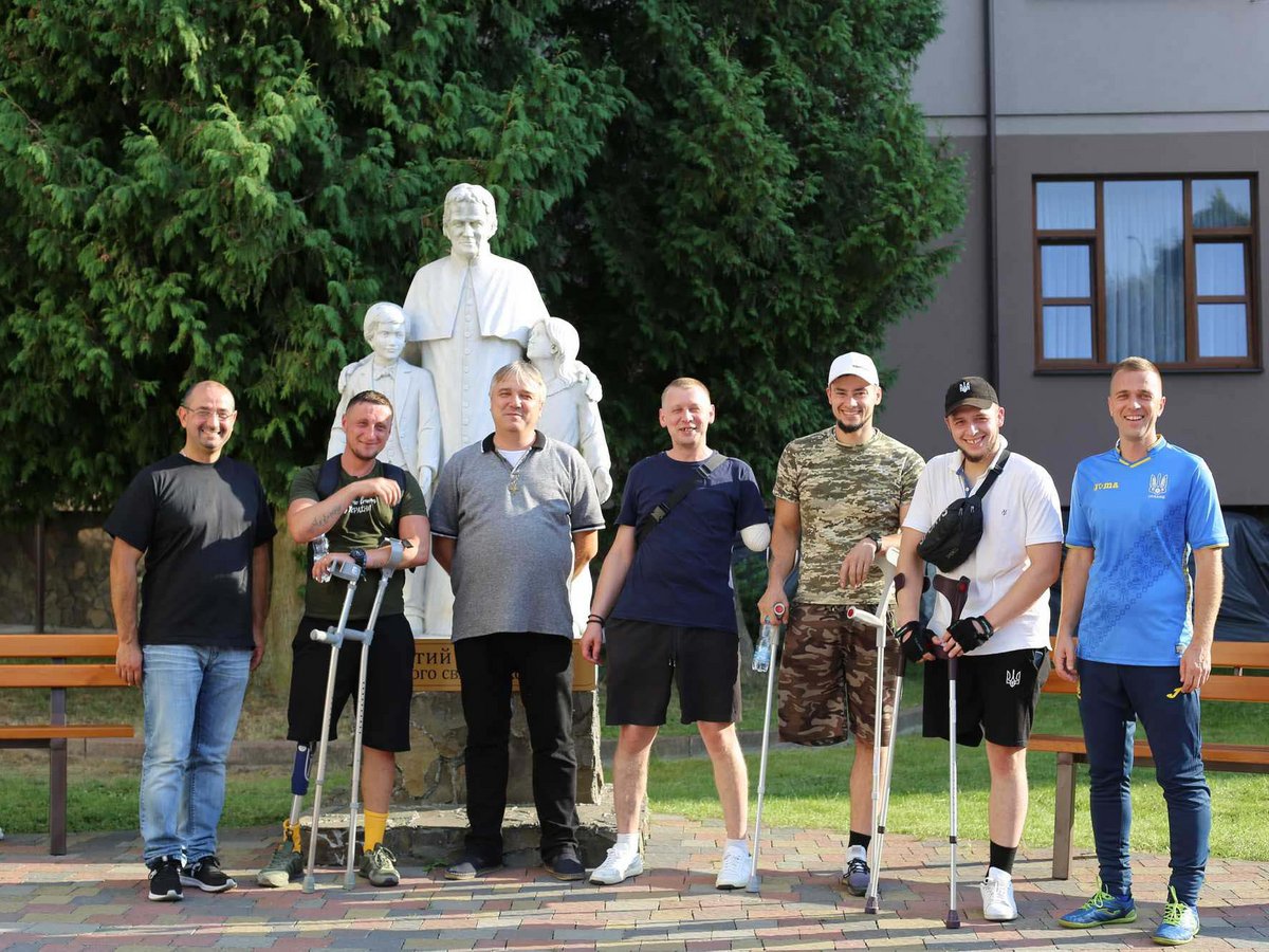 Eine Gruppe lächelnder Männer, einige mit Kriegsverletzungen und Gehhilfen oder Prothesen, steht draußen bei einer Statue.