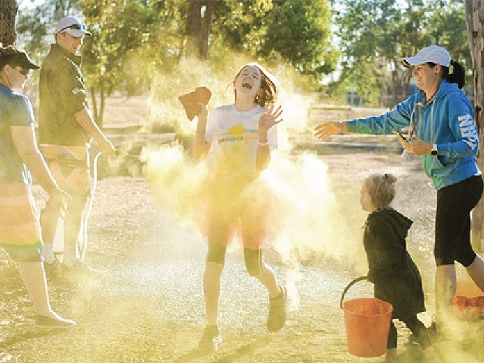 Eine Gruppe Menschen genießt ein Farbfestival im Freien, während gelbes Puder um ein lachendes Mädchen herum aufsteigt.