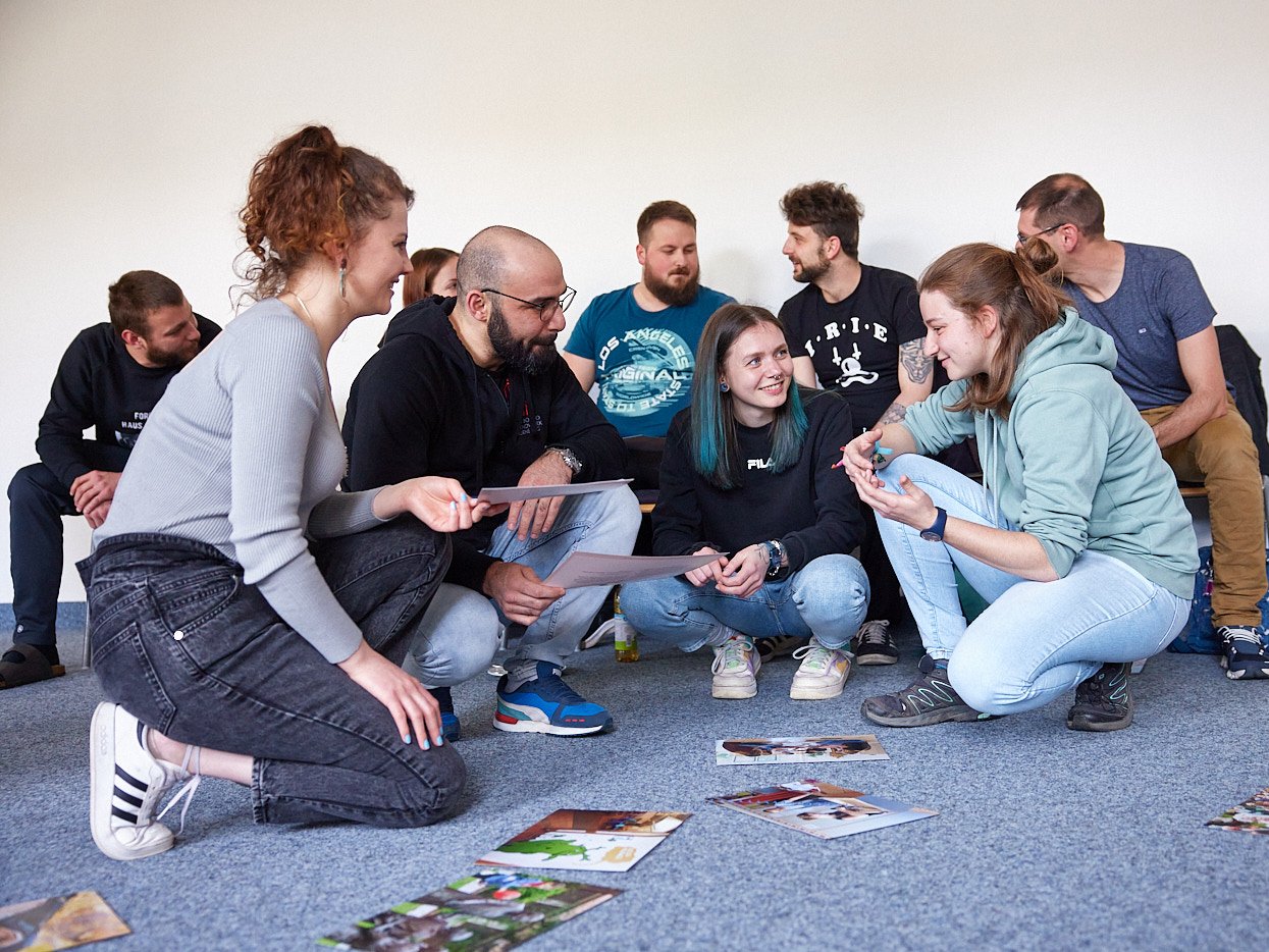 Gruppe Erwachsener bespricht Fotos und Dokumente auf dem Boden bei einem Workshop.