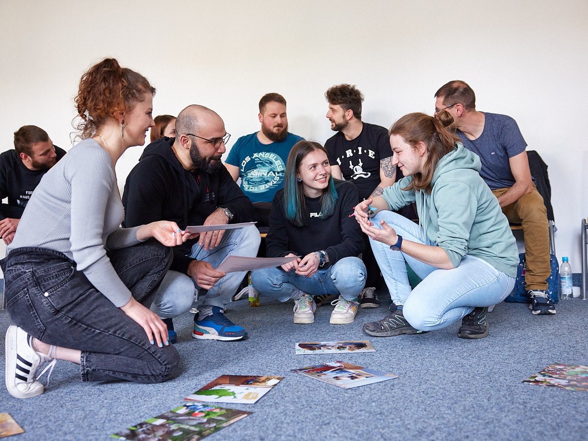 Gruppe Erwachsener bespricht Fotos und Dokumente auf dem Boden bei einem Workshop.