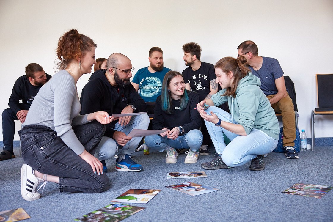 Gruppe Erwachsener bespricht Fotos und Dokumente auf dem Boden bei einem Workshop.