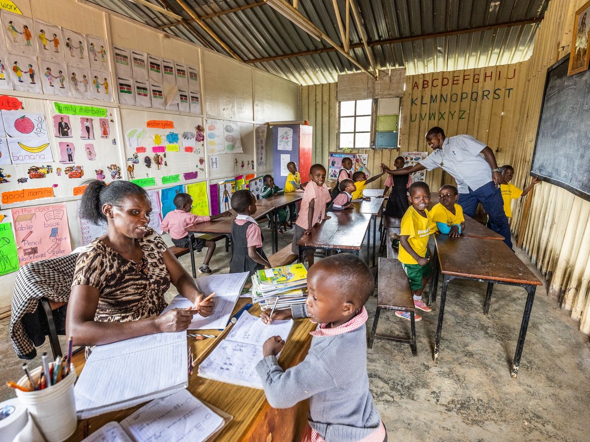 Ein lebhaftes Klassenzimmer mit lernenden Kindern und zwei Lehrern, umgeben von bunten Lernpostern.