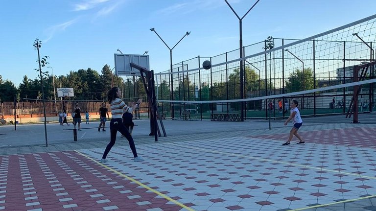 Zwei Frauen spielen Volleyball auf einem gepflasterten Außenplatz unter blauem Himmel, der Ball ist in der Luft.