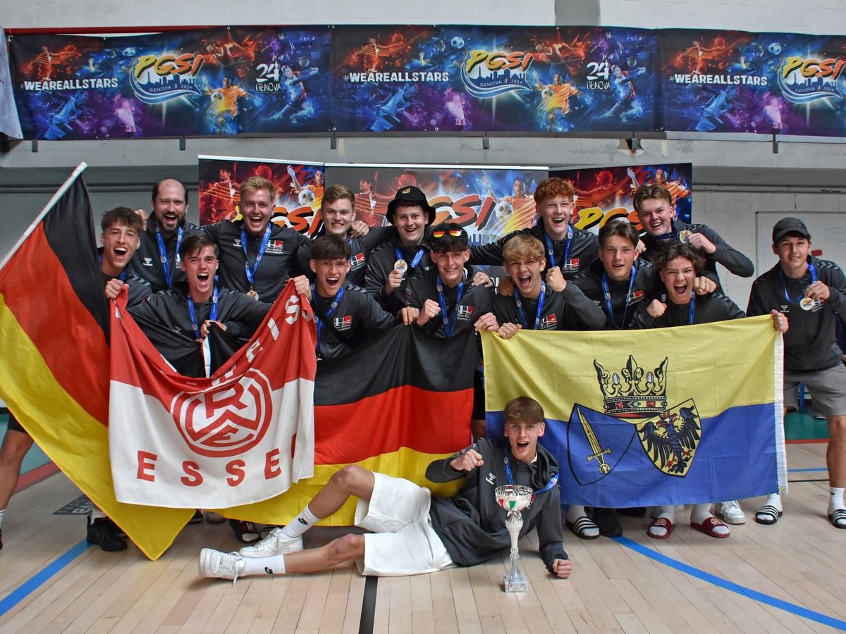 Eine lachende Gruppe junger Männer und ein Erwachsener feiern in einer Sporthalle mit Deutschland- und RW Essen-Fahne und einem Pokal.