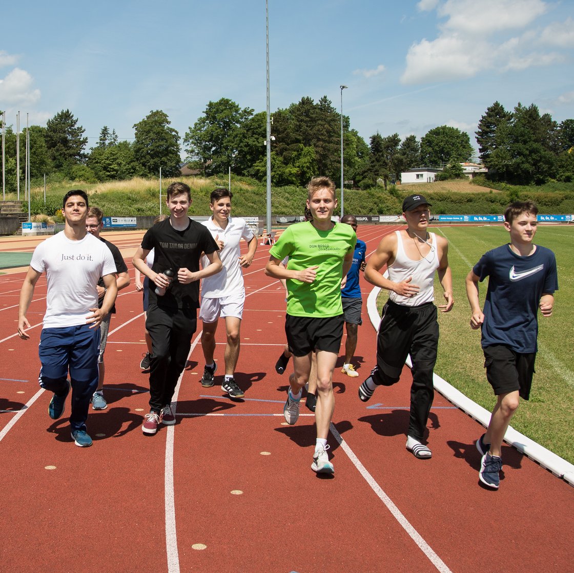 Vielfältige Gruppe junger Menschen läuft an einem sonnigen Tag auf einer roten Leichtathletikbahn.