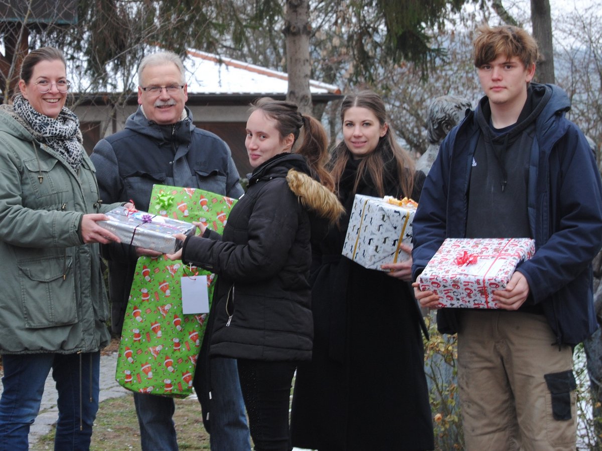 Fünf Personen präsentieren draußen verpackte Geschenke und lächeln in die Kamera.