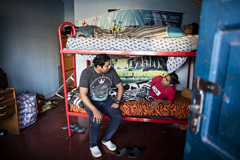 Ein Mann sitzt an einem Etagenbett und spricht mit einem Liegenden, während eine dritte Person auf dem oberen Bett ruht.