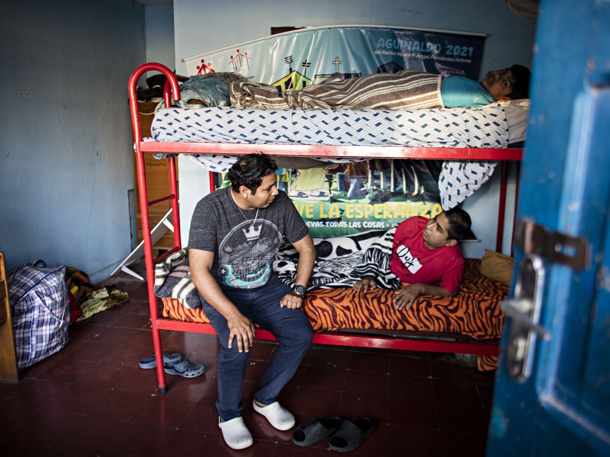 Ein Mann sitzt an einem Etagenbett und spricht mit einem Liegenden, während eine dritte Person auf dem oberen Bett ruht.