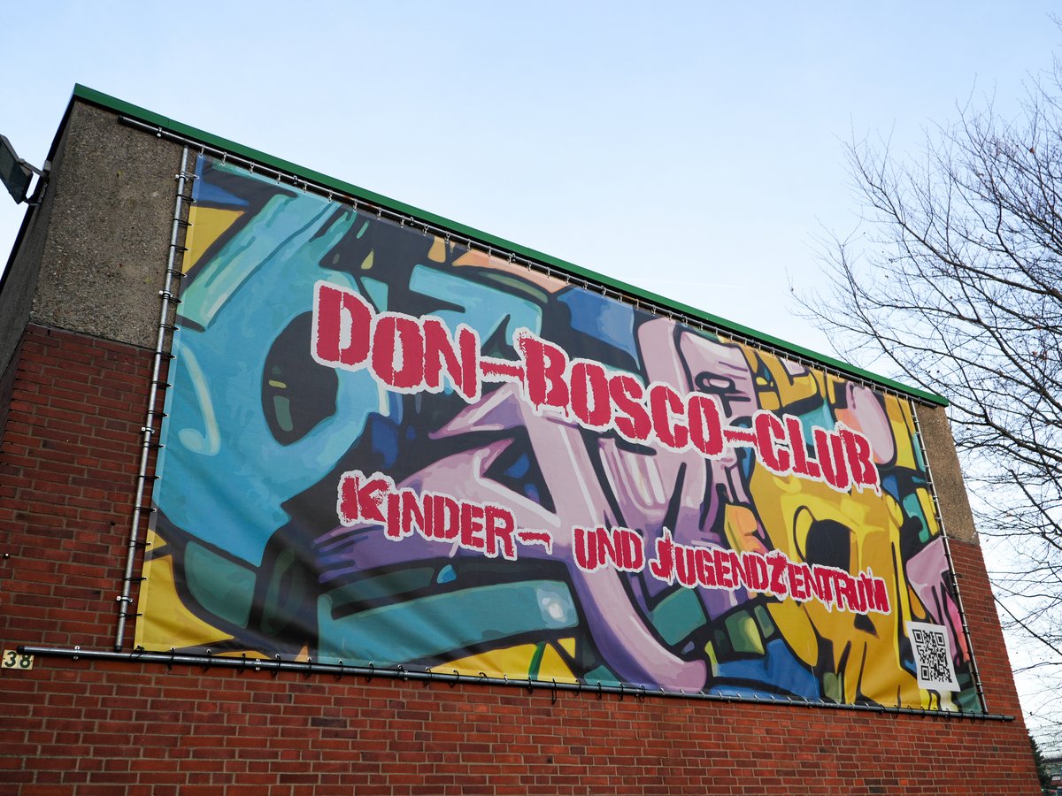 Buntes Don-Bosco-Club Kinder- und Jugendzentrum Banner mit QR-Code an einem Backsteingebäude.