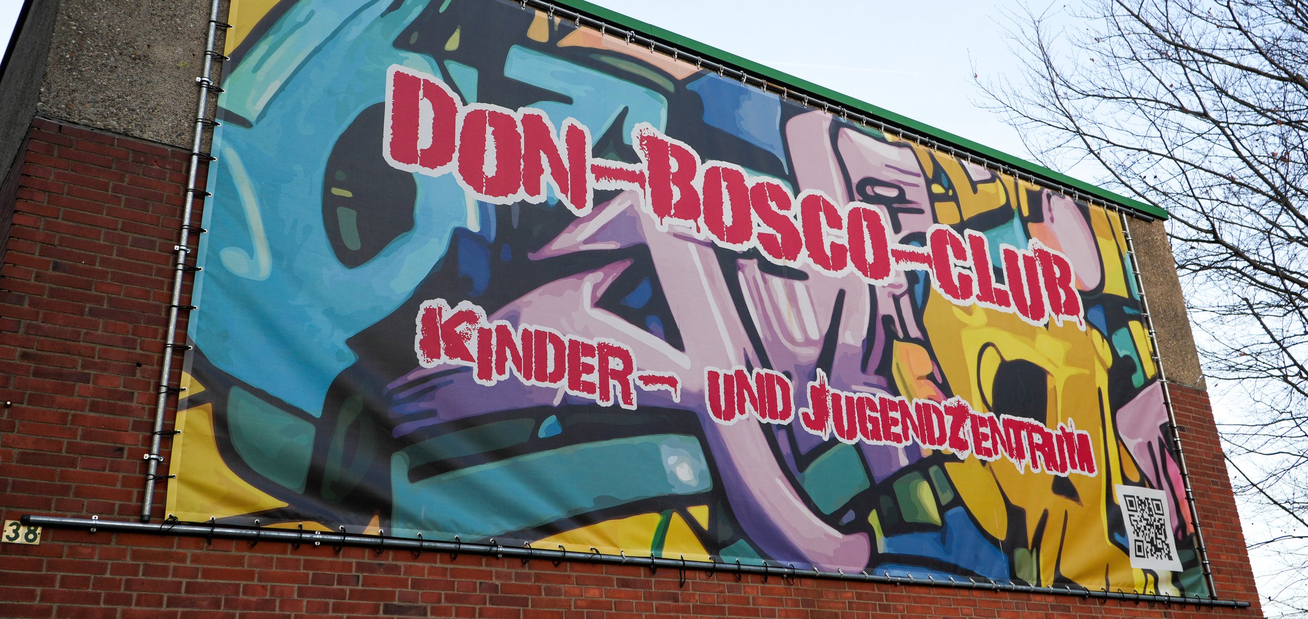 Buntes Don-Bosco-Club Kinder- und Jugendzentrum Banner mit QR-Code an einem Backsteingebäude.