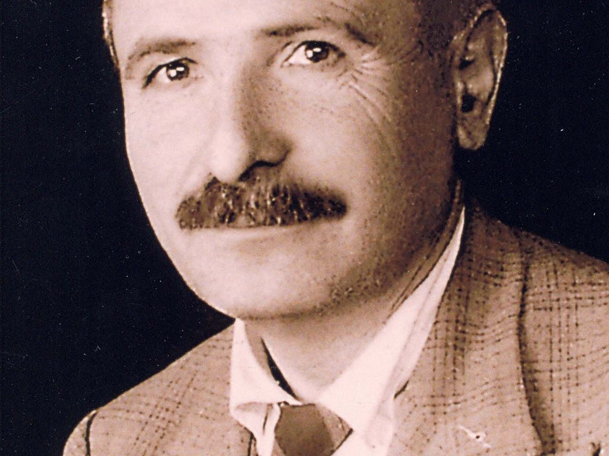 Vintage Sepia-Porträt eines Mannes mit Schnurrbart und kurzen Haaren, kariertes Sakko tragend, seitlich blickend.