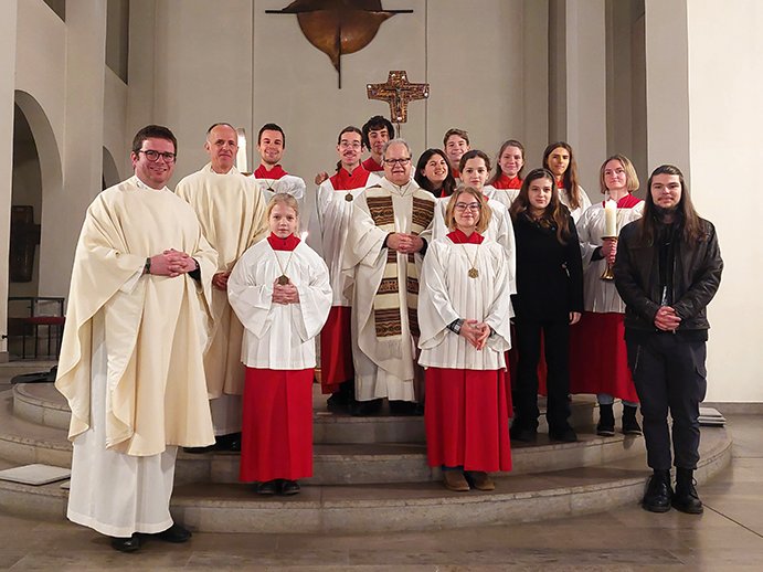 Eine Gruppe von Priestern und Messdienern in einer Kirche, mit einem Kruzifix im Hintergrund.