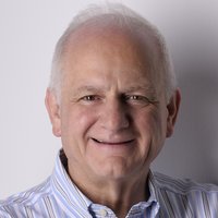 Porträt eines lächelnden älteren Mannes mit weißen Haaren und einem blau-weiß gestreiften Hemd.