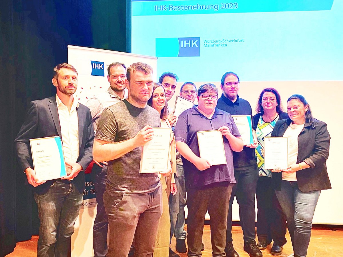 Eine Gruppe von Auszubildenden und Ausbildern bei der IHK-Bestenehrung 2023 hält Urkunden vor einem Bildschirm.