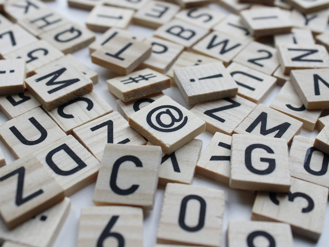 Nahaufnahme eines Haufens verstreuter Holzplättchen mit Buchstaben, Zahlen und Symbolen auf weißem Hintergrund.