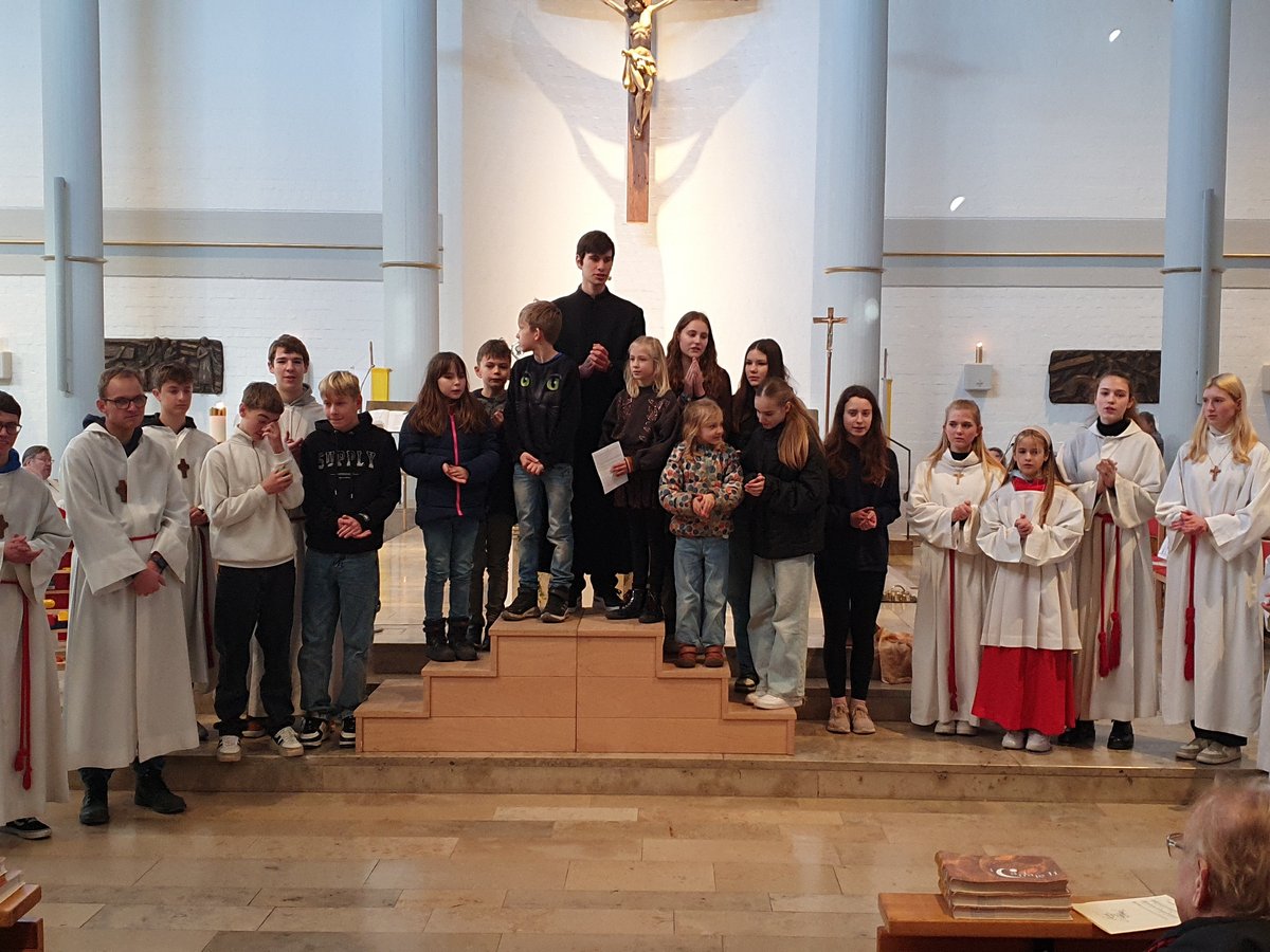 Junge Menschen, einige in weißen Gewändern, stehen in einer Kirche vor einem Kruzifix und einer Osterkerze.
