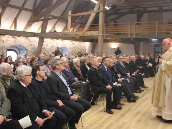 Kardinal spricht zu einem sitzenden Publikum in einem historischen Saal mit sichtbaren Holzbalken.