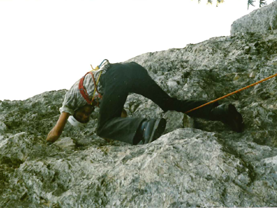 Ein Kletterer mit Helm und Gurt steigt eine felsige Wand hinauf, mit einem Sicherheitsseil, das nachfolgt.