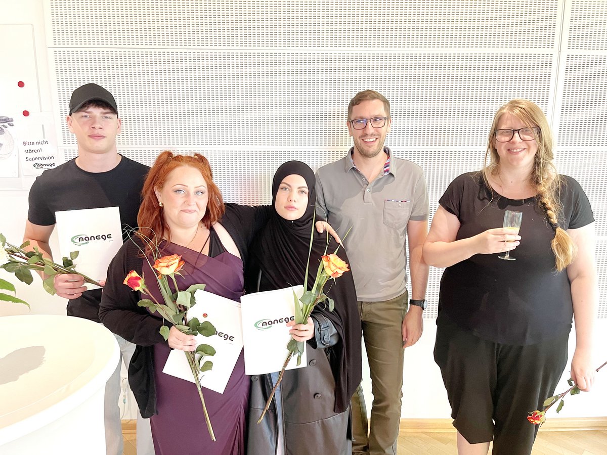 Fünf lächelnde Personen, drei mit "nanege"-Zertifikaten und Rosen, eine mit Getränk, feiern einen Erfolg.