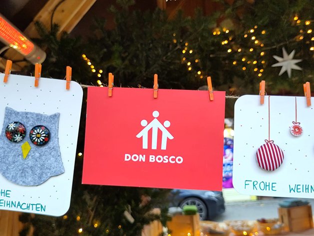 Drei Weihnachtsdekorationen: Eine Filzeule, ein rotes Don Bosco Schild und eine Ornamentkarte, alle mit 'Frohe Weihnachten'.