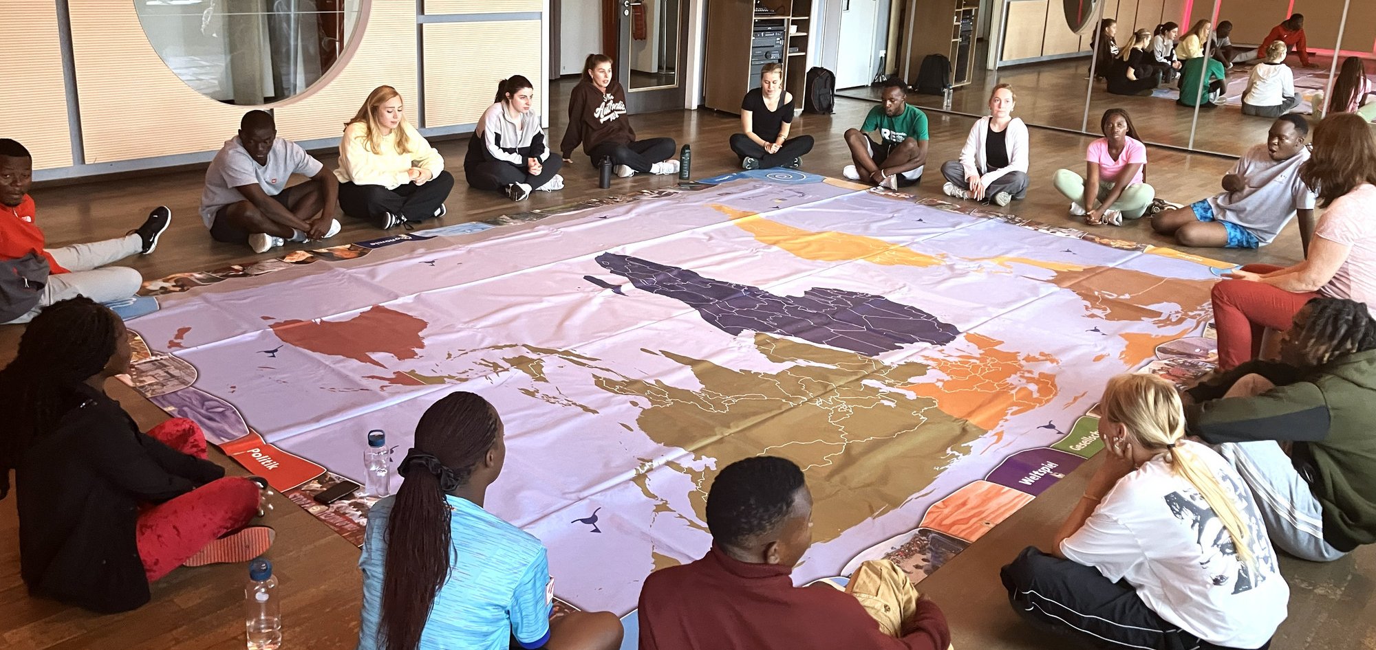 Vielfältige junge Erwachsene sitzen auf dem Boden um eine große Weltkarte und nehmen an einer interaktiven Bildungsaktivität teil.