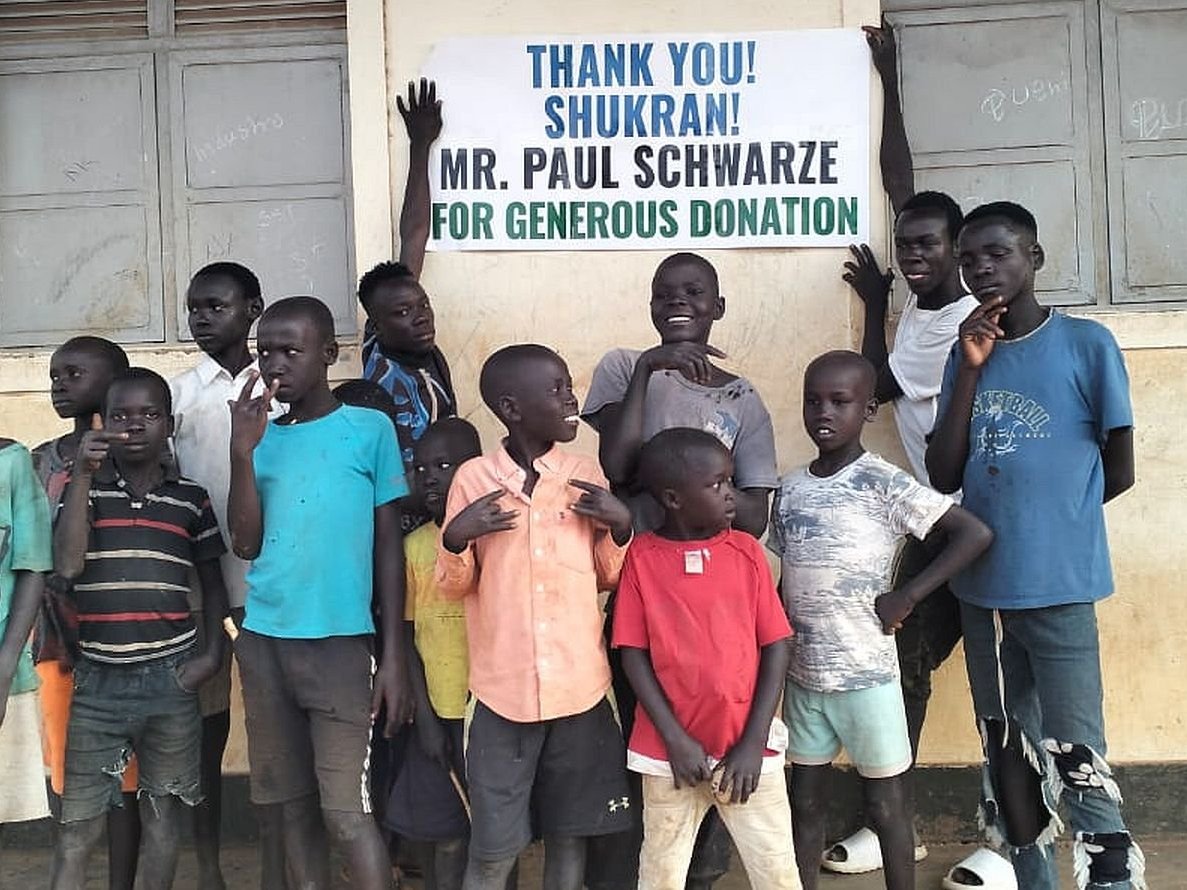 Kinder stehen vor einer Schule und halten ein Schild mit der Aufschrift "Danke" hoch.