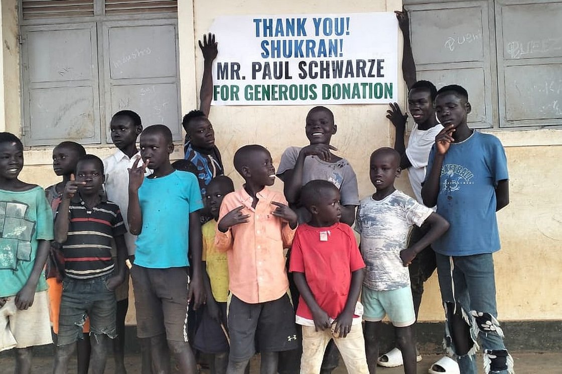 Kinder stehen vor einer Schule und halten ein Schild mit der Aufschrift "Danke" hoch.