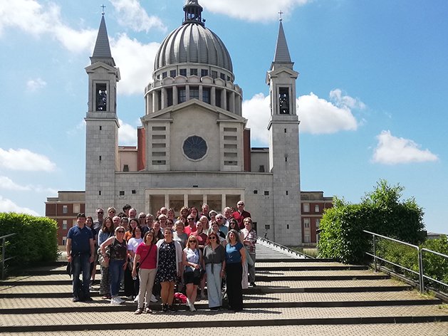 Große Gruppe von Menschen posiert auf Stufen vor einer prächtigen Kirche mit Kuppel und Türmen an einem sonnigen Tag.