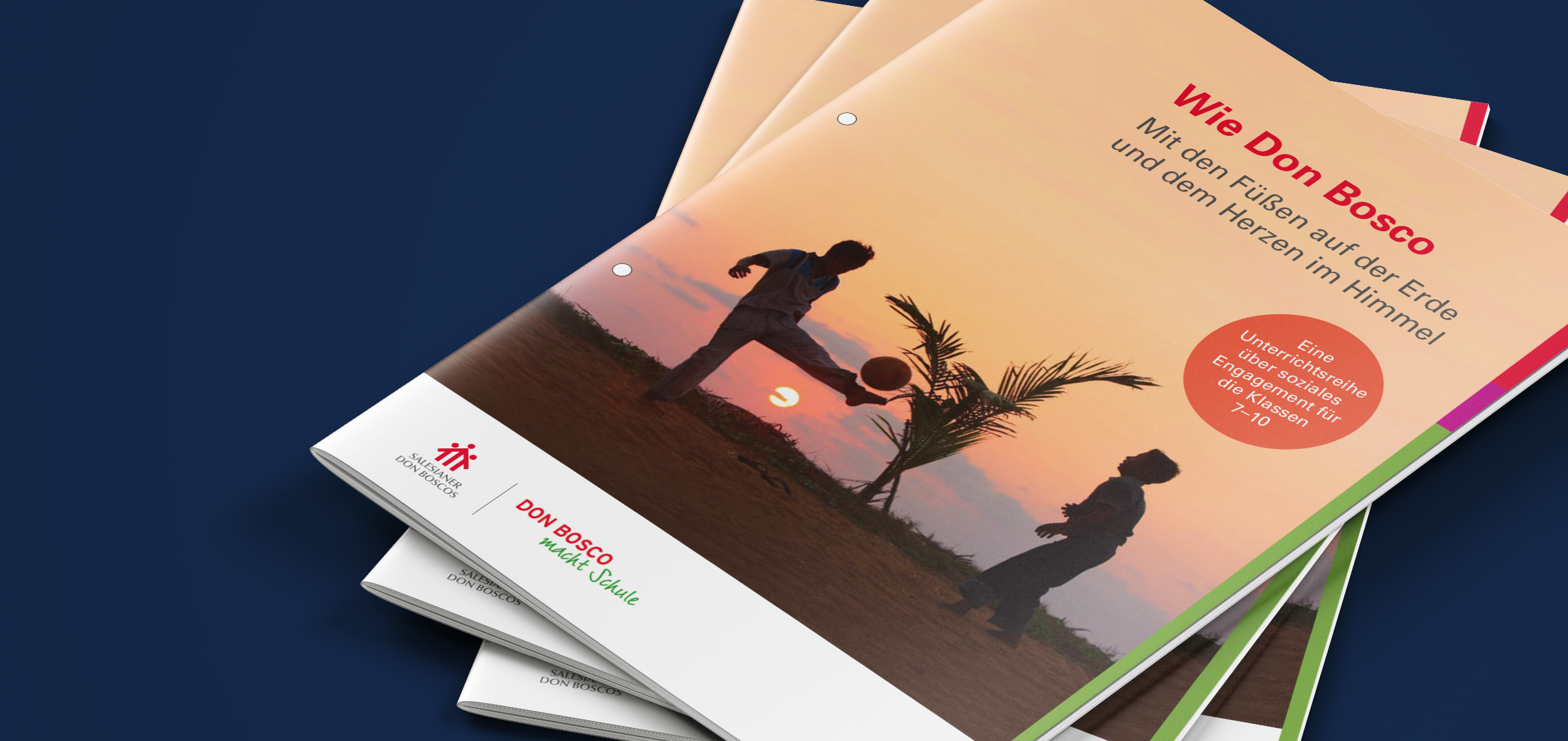 Broschürenstapel. Das Cover der obersten Broschüre zeigt den Titel 'Wie Don Bosco' und Silhouetten, die bei Sonnenuntergang Ball spielen.