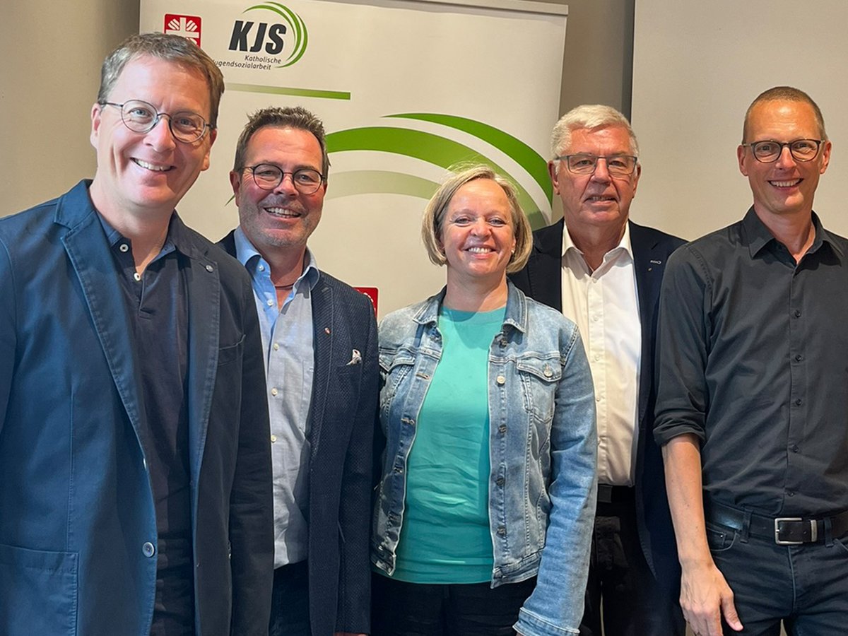 Fünf lächelnde Personen, vier Männer und eine Frau, vor einem Banner der Katholischen Jugendsozialarbeit (KJS).