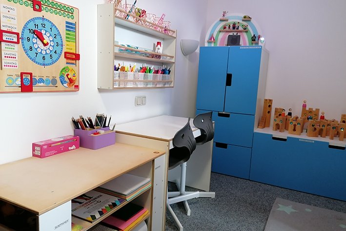 Ein heller Lernbereich für Kinder mit Holzkalender, Zeichentisch, blauen Schränken und Holzspielzeug.