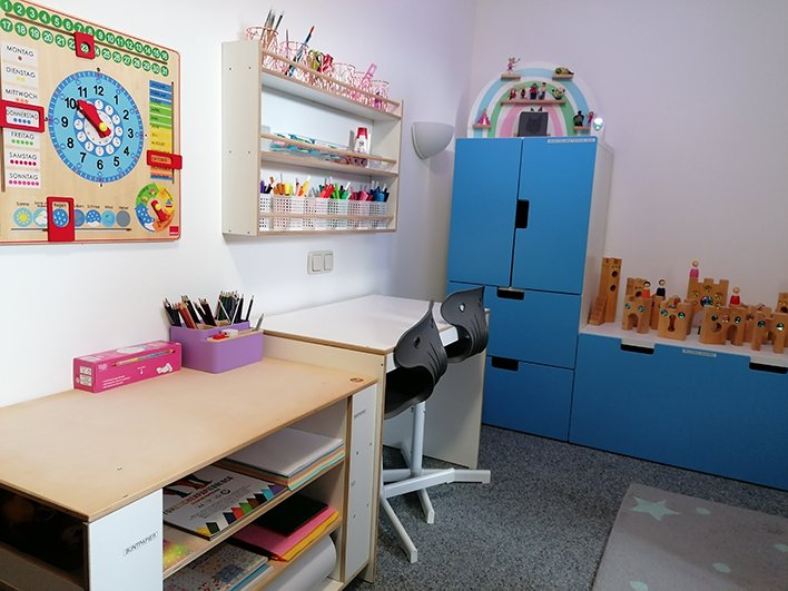 Ein heller Lernbereich für Kinder mit Holzkalender, Zeichentisch, blauen Schränken und Holzspielzeug.