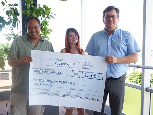 Drei Personen überreichen einen Scheck von Bayernhafen Rückwind über 1.500 Euro an das Don Bosco Jugendwerk Nürnberg für eine Freizeit am Meer.