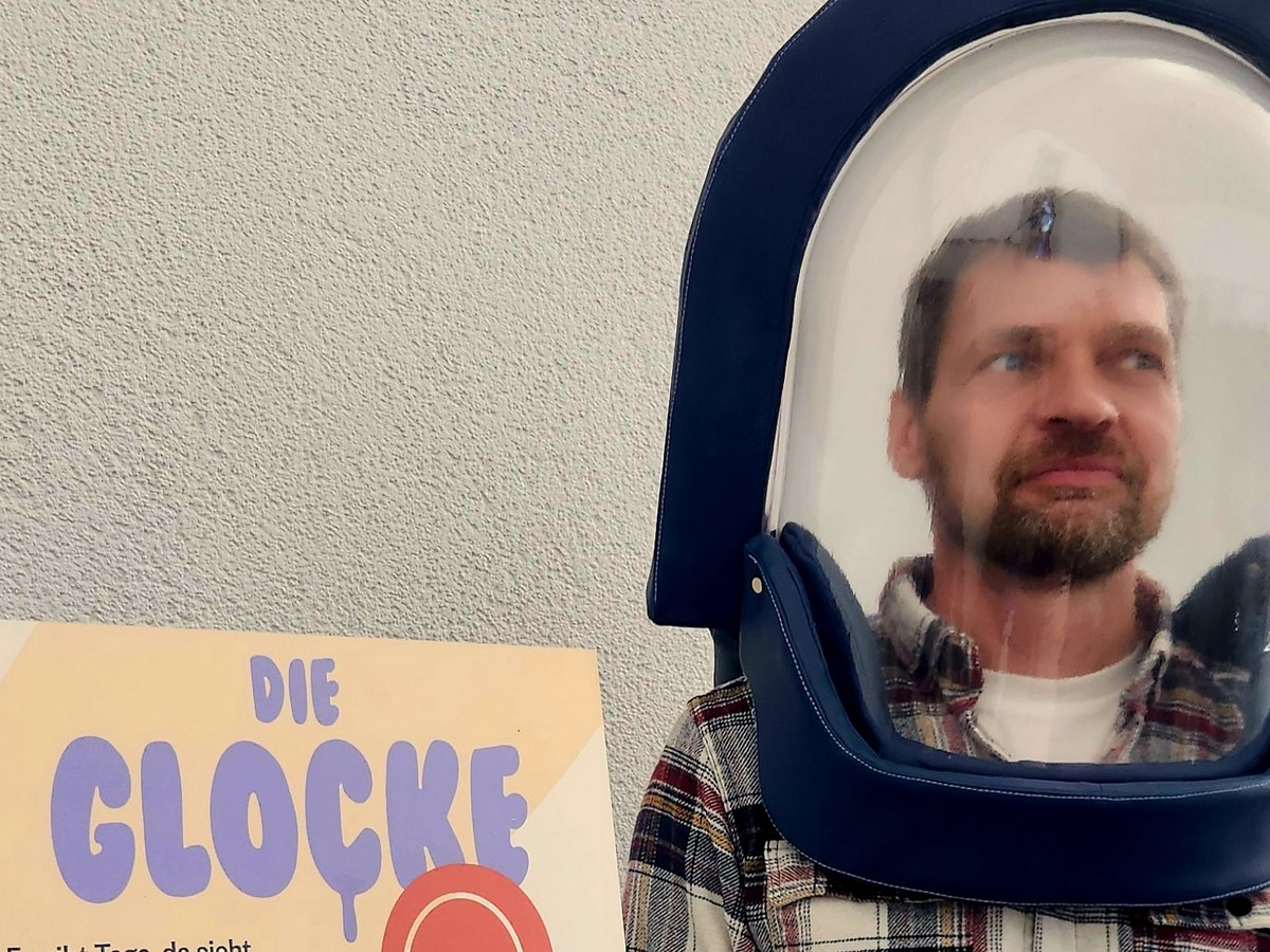 Mann mit blauem Helm und durchsichtigem Visier blickt nach rechts, daneben ein Plakat mit der Aufschrift 'DIE GLOCKE'.