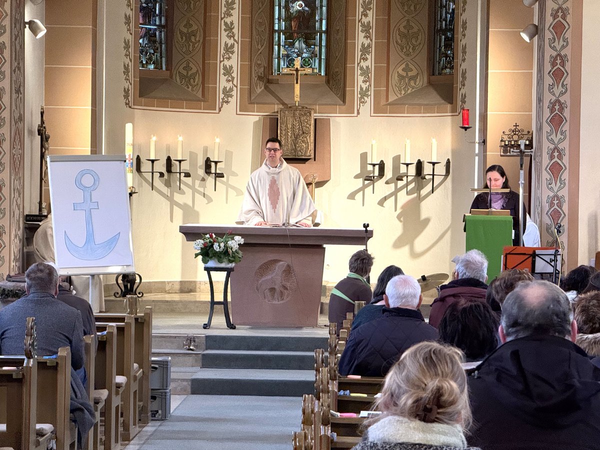 Priester hält Gottesdienst in Kirche mit Gemeinde und Flipchart mit blauem Anker.