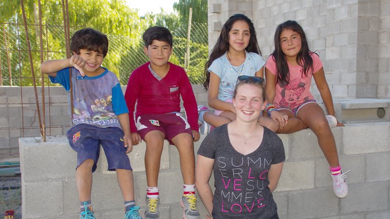 Fünf lächelnde Personen, eine junge Frau und vier Kinder, posieren auf einer Betonmauer, einige sitzend, eine stehend.