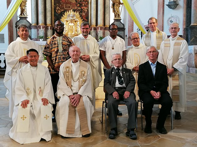 Diverse Priester und Männer verschiedener Altersgruppen in einer Kirche.