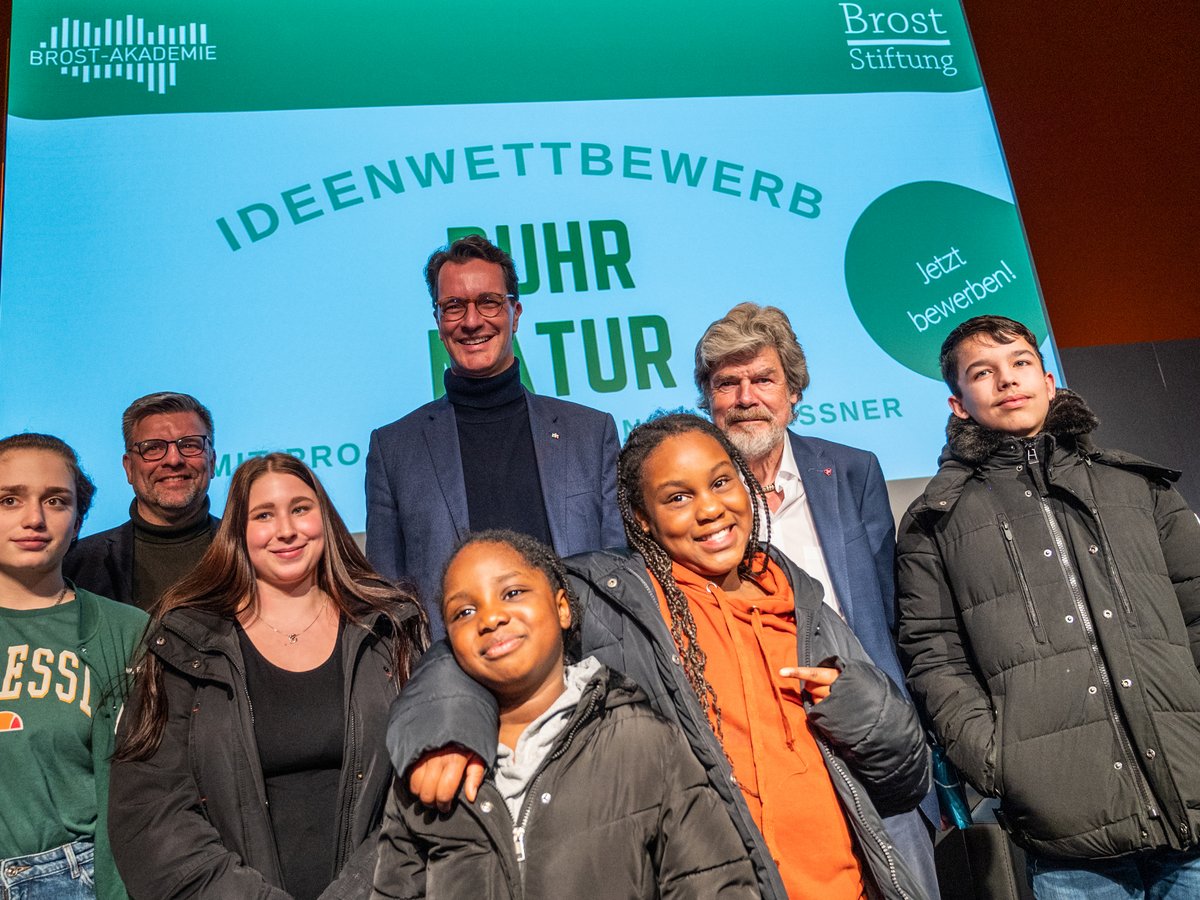 Eine Gruppe von Erwachsenen und Jugendlichen posiert lächelnd vor einer Leinwand des Brost-Akademie Ideenwettbewerbs.