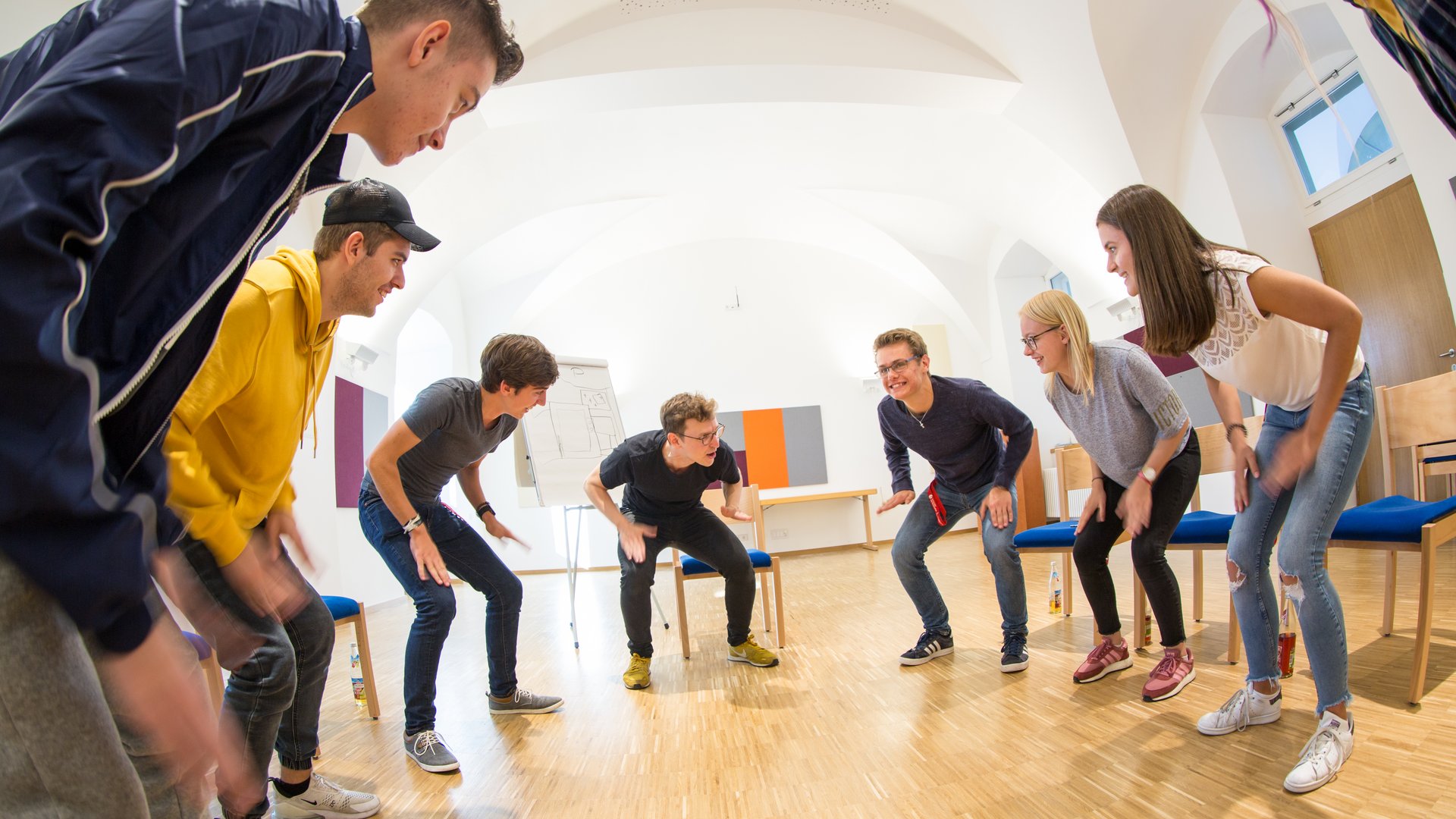 Junge Erwachsene in einem Kreis, kauernd und nach innen blickend bei einer lebhaften Teamaktivität.