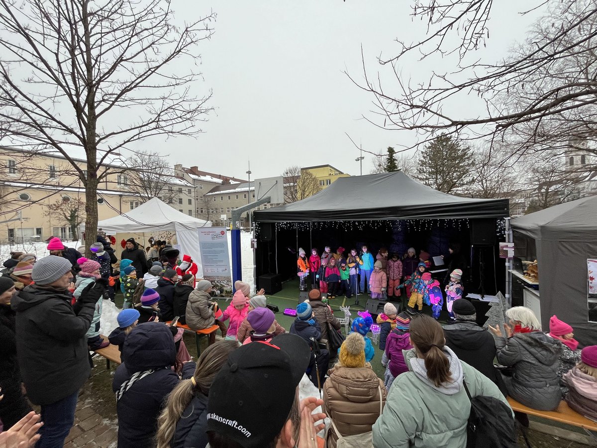 Kinderchor tritt auf einer Bühne bei einem winterlichen Fest auf dem Campus Don Bosco auf. Publikum schaut in warmer Kleidung zu.