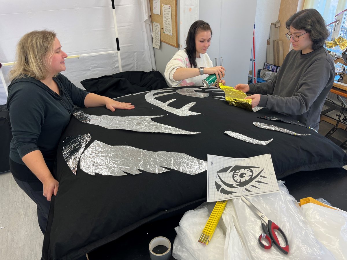 Drei Personen basteln ein Augendesign auf schwarzem Stoff mit Silber- und Goldfolie.