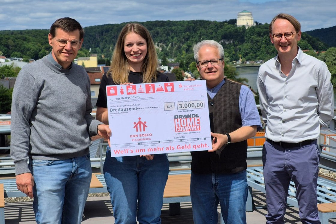 Vier lächelnde Personen mit einem großen Scheck über 3.000 EUR an Don Bosco Regensburg von Brandl Home Company.