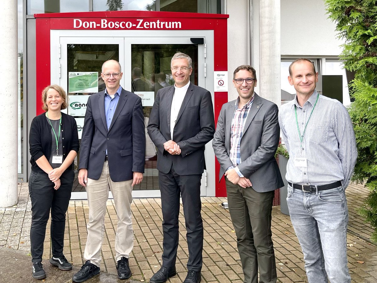 Fünf lächelnde Personen, darunter eine Frau und ein Priester, vor dem Gebäude des Don-Bosco-Zentrums.