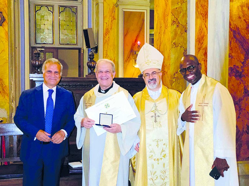 Vier lächelnde Männer, darunter ein Bischof, zwei Priester und ein Mann im Anzug, in einer Kirche, ein Priester hält eine Auszeichnung.