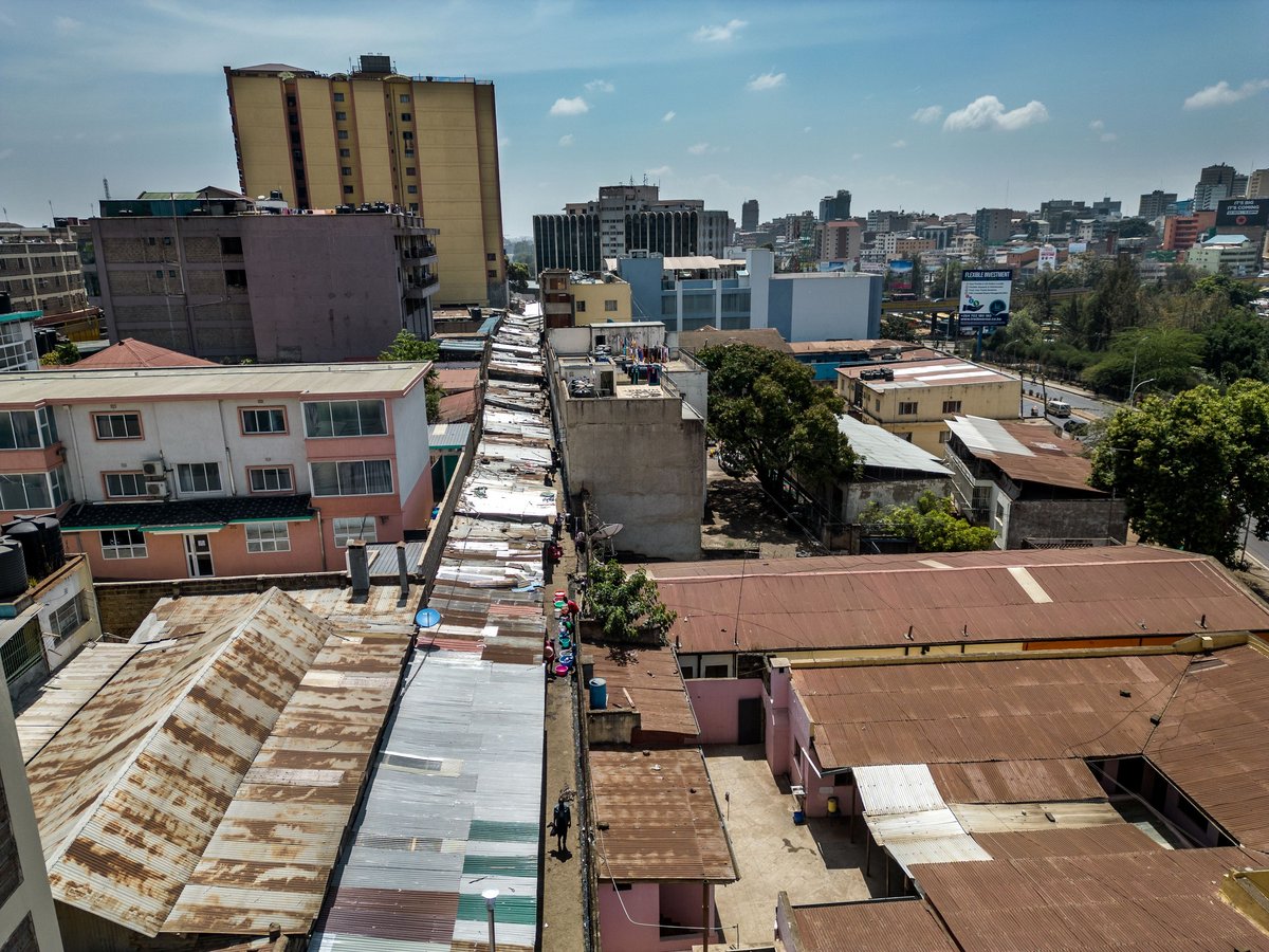 Ansicht von oben auf Nairobi: Wellblechdächer, belebte Gasse, diverse Gebäude, klarer blauer Himmel.