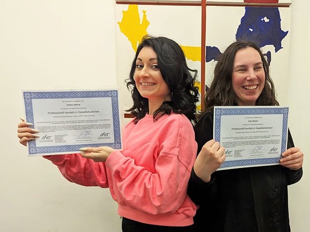 Kristina Moine und Anja Prestar lächeln und halten Zertifikate für den Umgang mit Gewaltsituationen.