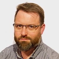 Porträt eines Mannes mit Bart und Brille im gestreiften Hemd.