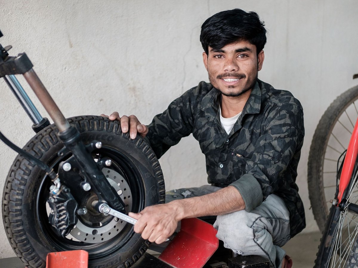 Ein lächelnder Mann in Tarnkleidung arbeitet mit einem Schraubenschlüssel am Vorderrad eines Rollers.
